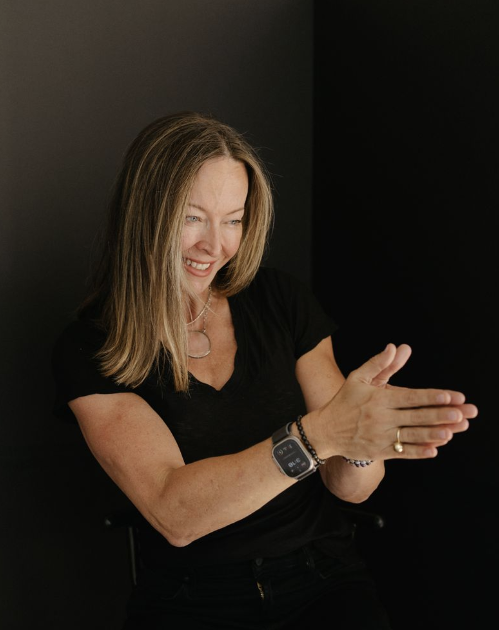 Anese Cavanaugh seated with her hands pressed together, smiling gently against a dark backdrop