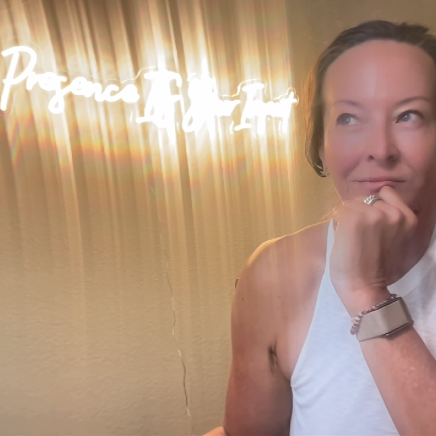 Anese resting her chin on her hand beside a glowing neon sign that reads 'Presence is your power.'