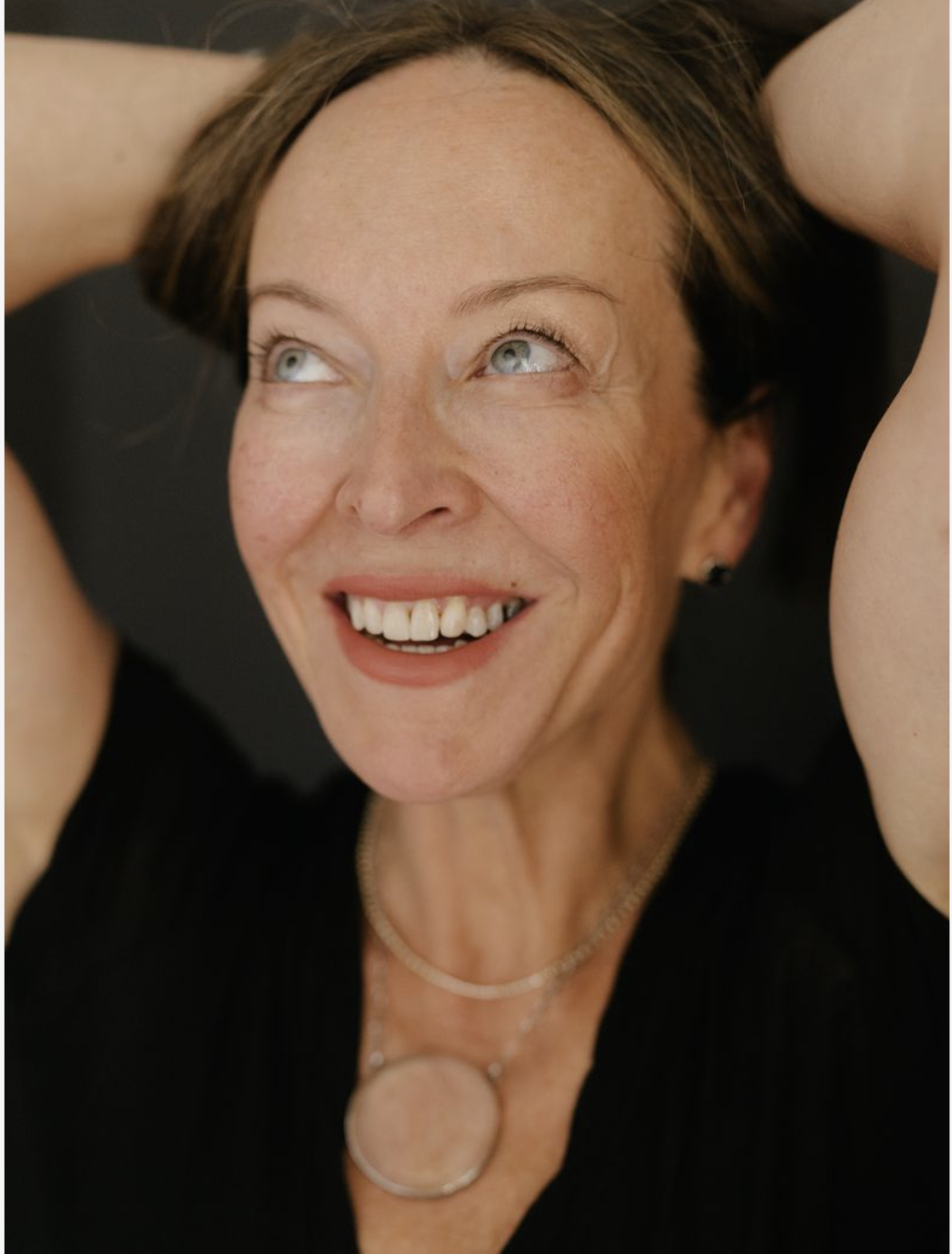 Anese Cavanaugh laughing with her hands in her hair, wearing a black tee against a dark backdrop