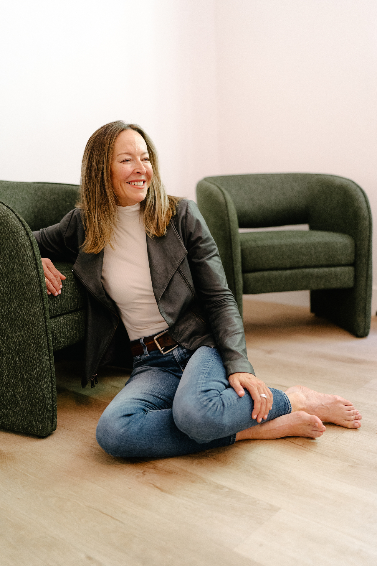 Anese sitting on the floor beside a sculptural green armchair, laughing
